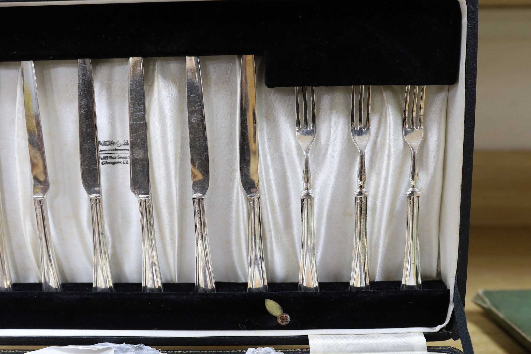 A cased dessert service containing six gilt and fruit decorated plates and a set of knives and forks